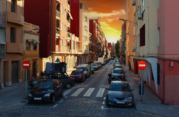 Cars parked on a narrow street near house and residential buildings. Parking with cars in a residential area of a European city. Narrow one-way road in city among high-rise buildings with palm trees.