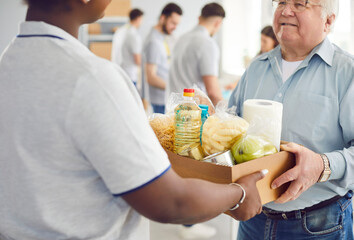 African american volunteer working at charity center giving free food donations for mature man in...