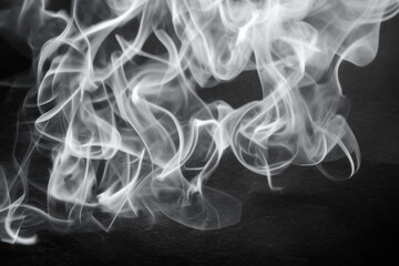 Elegant smoke swirls create a mesmerizing pattern against a dark background in a low-light environment
