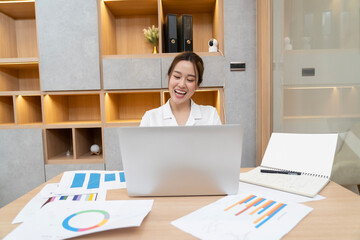A woman is sitting at a desk with a laptop open in front of her. She is smiling and she is enjoying...
