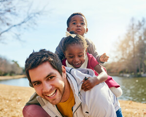 Fototapeta premium Father, children and adoption with piggyback, smile and field for fun and playing in park. Vacation, interracial family and kids with bonding, carry and joy together for summer holiday confidence