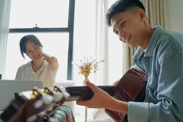 Two Asian people learning guitar at home