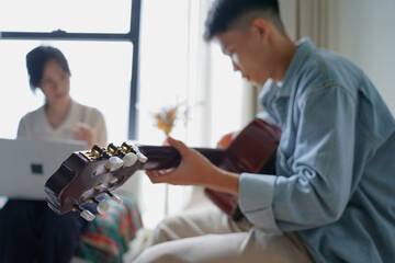 Two Asian people learning guitar at home