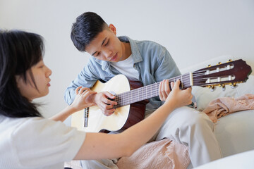 Two Asian people learning guitar at home