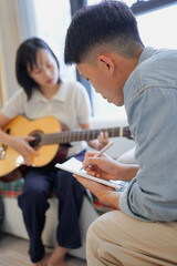 Two Asian people learning guitar at home