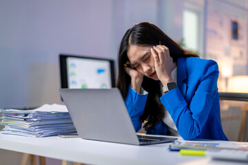 A woman in a blue jacket is sitting at a desk with a laptop open