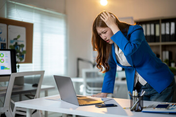 A woman in a blue jacket is sitting at a desk with a laptop