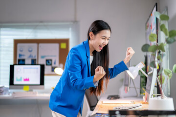 A woman in a blue jacket is celebrating with her hands up in the air