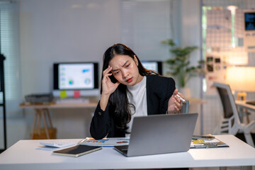 A woman is sitting at a desk with a laptop and a stack of papers