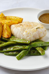 Delicious white fish served with green beans and roasted potatoes on a white plate