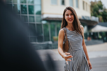 Fototapeta premium A joyful young woman wearing a striped dress reaches out for a handshake on a city street, radiating warmth and friendliness.