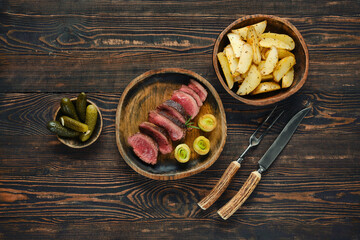 Elegant dinner setting with sliced meat, roasted potatoes, and pickles on rustic wooden table