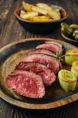 Grilled steak served with leeks and potato wedges on a rustic wooden table