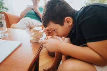 A cozy home scene showcasing a grandmother knitting a vest while her grandson intently plays with building blocks on the table.