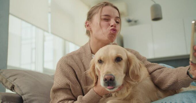 A young woman taking a selfie while playfully puckering her lips and cuddling her golden retriever, capturing a fun and heartwarming moment of bonding with her pet
