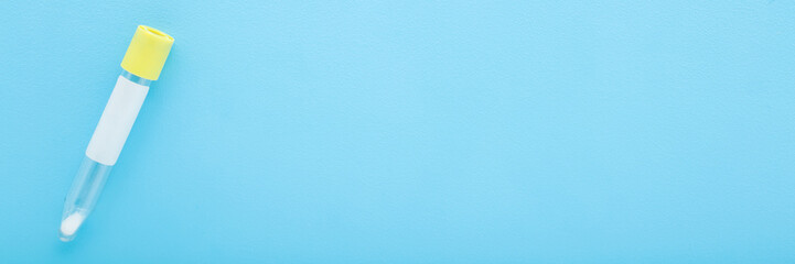 Empty transparent plastic tube for urine or other analysis test on light blue table background. Pastel color. Healthcare concept. Closeup. Empty place for text. Wide banner. Top view.