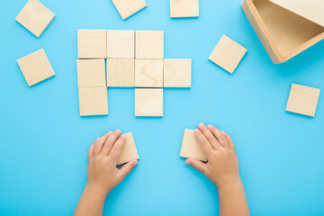 Baby boy hands playing and putting together wooden puzzle square pieces on light blue table background. Pastel color. Closeup. Point of view shot. Children development. Top down view.