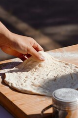 A chef skillfully sets up fresh pizza dough on a wooden surface, dusted with flour. The dough is...