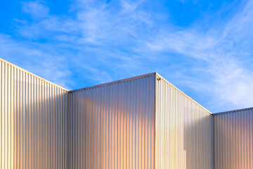 Industrial Warehouse Building with Metal Corrugated Steel Exterior Wall and Geometric Aluminium Roof against Blue Sky Background, Low Angle view 