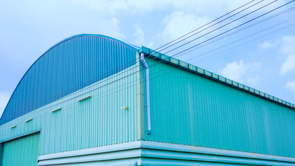 Fototapeta premium The old green corrugated steel industrial warehouse building with dome roof and cable lines against pale sky background, low angle and perspective side view