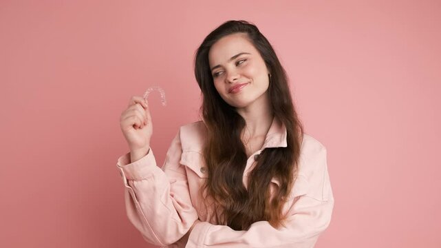 Happy young woman showing invisible braces in pink studio