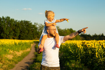 Young man with glasses holds a child on his shoulders and points with his hand to something on a...