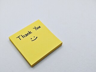 Thank you with smile icon on yellow sticky note, isolated on a grey background.