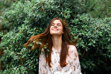 joyful woman standing in front of lush greenery with windblown hair