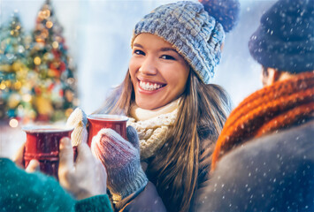 Young woman enjoying hot red wine with friends at a winter scene with christmas trees 