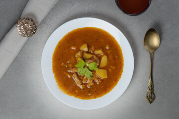 Delicious bowl of Hungarian Szeged goulash with aromatic spices served on a white plate alongside a refreshing drink