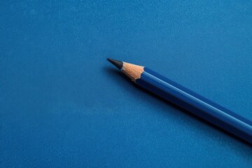 Blue pencil resting on a textured dark blue surface in a minimalistic setting