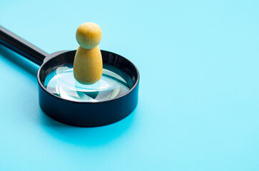 A wooden figure doll standing on top of magnifying glass with customizable space for text or ideas