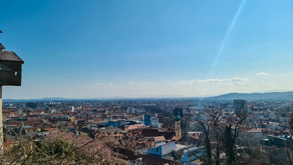 Scenic aerial view of Graz seen from Schlossberg, Styria, Austria, Europe. Unesco world heritage site with red-roofed buildings. City is nestled amidst rolling hills. Mur River winds through old town