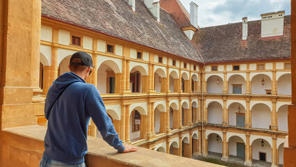 Rear view of tourist man looking at lavish interior courtyard of Schloss Eggenberg in Graz, Styria, Austria, Europe. Baroque palace complex as part of Unesco world heritage site. Tourist destination