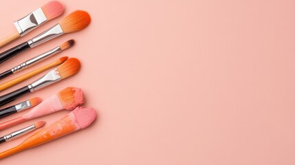 Various paintbrushes covered in pink and orange paint on pastel background
