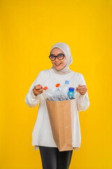 asian hijab woman sorting plastic bottle standing in isolated plain yellow background