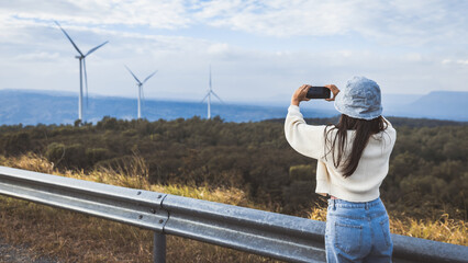 Asian woman traveler with mobile phone relax and travel with wind turbine on mountain background Thailand