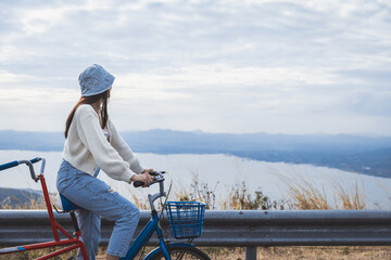 Asian woman traveler with bicycle relax and travel with wind turbine on mountain background Thailand