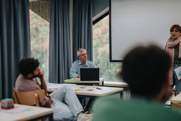 An elderly professor leads a diverse group of attentive students in a modern classroom environment, fostering learning and collaboration.