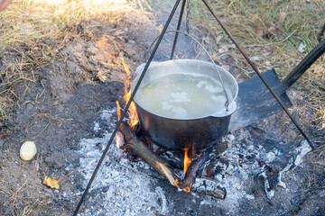 Cook porridge on a hike. Add firewood and coals with a shovel. Cooking food on a campfire hiking....
