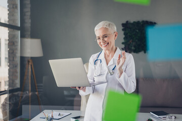 Photo of aged woman qualified doctor video call laptop wear white coat workplace office indoors