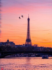 Obraz premium A serene sunset view of the Eiffel Tower with birds flying over the Seine River.