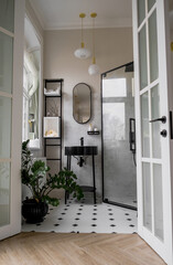 A modern bathroom with a black sink stand, a round sink, a black oval mirror, white and black tiled floor, and a shower stall.