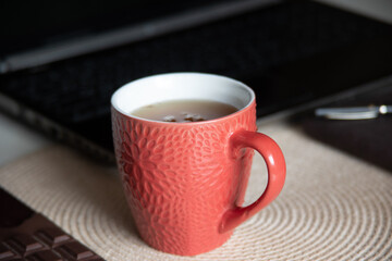 The image shows a red ceramic mug with a textured floral pattern, filled with tea. 