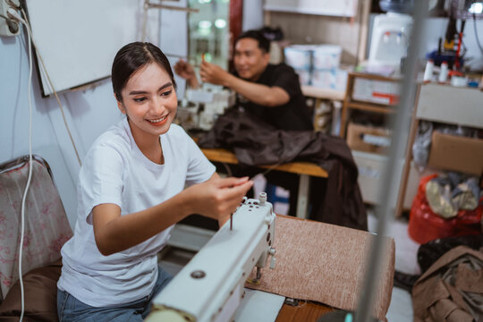 female tailor setting the yarn at sewing machine with the male tailor working at the background at window treatments production house