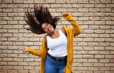 Smile, girl and dancing with hair shake for playful movement, energy and fun celebration of fashion winner. Happy, woman and rhythm for success, freedom and deal achievement on brick wall background