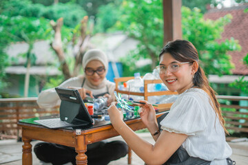 smiling asian woman painting upcycle plastic bottle with friend