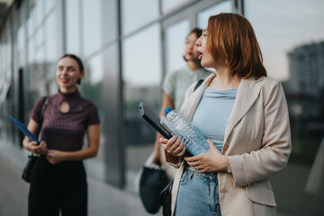 Group of business people walking outdoors, engaged in conversation after a successful meeting. They appear confident and relaxed, holding notebooks and water bottles.