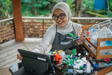 hijab woman making plastic bottle craft using tutorial from tablet