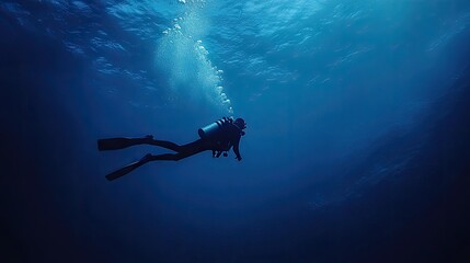 A lone scuba diver swims gracefully beneath the surface of a calm, deep blue ocean, creating a sense of adventure and peaceful exploration.